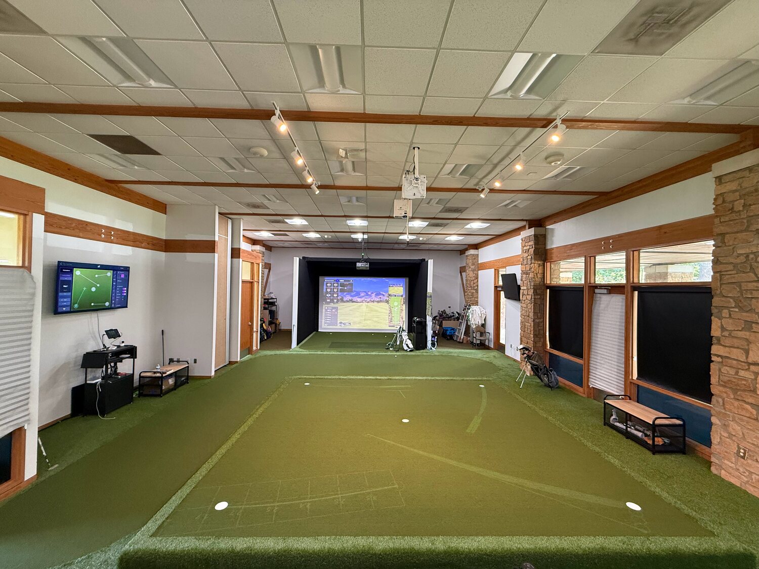 First Tee of Central Arkansas: a raised putting green with projected putting lines, leading to a simulator bay at the far end of the room