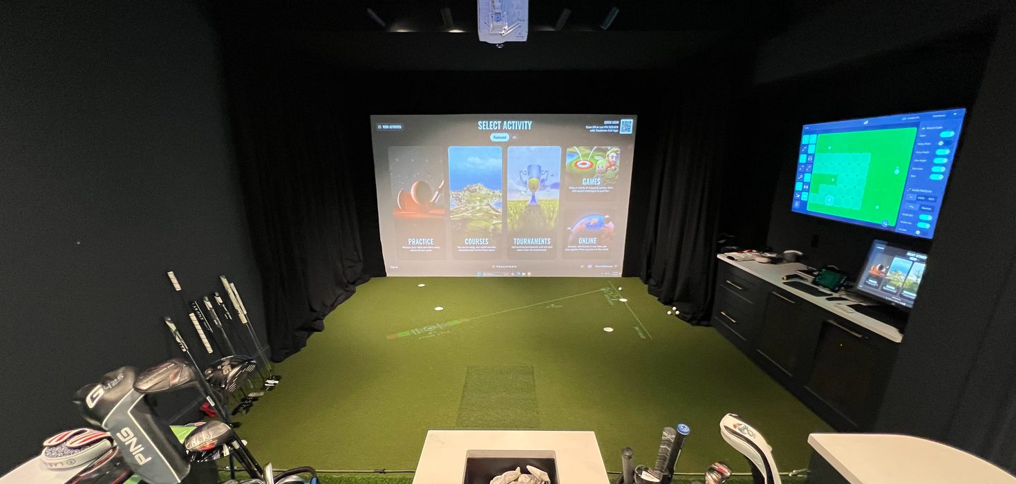 Home golf room with a simulator screen, a wall display, a putting green and club storage