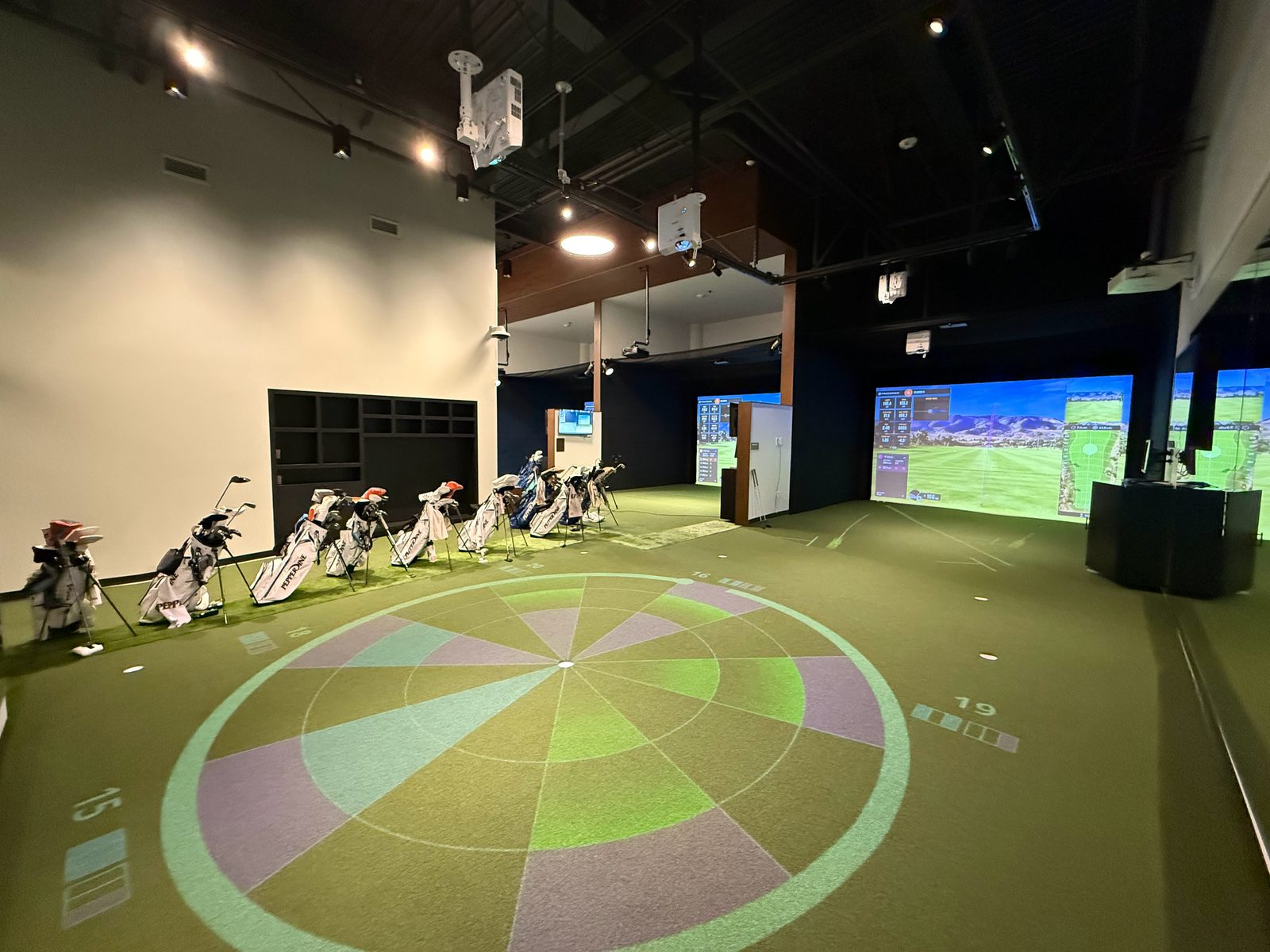 Pepperdine golf facility: simulator bays in use beside a putting green with a projected target
