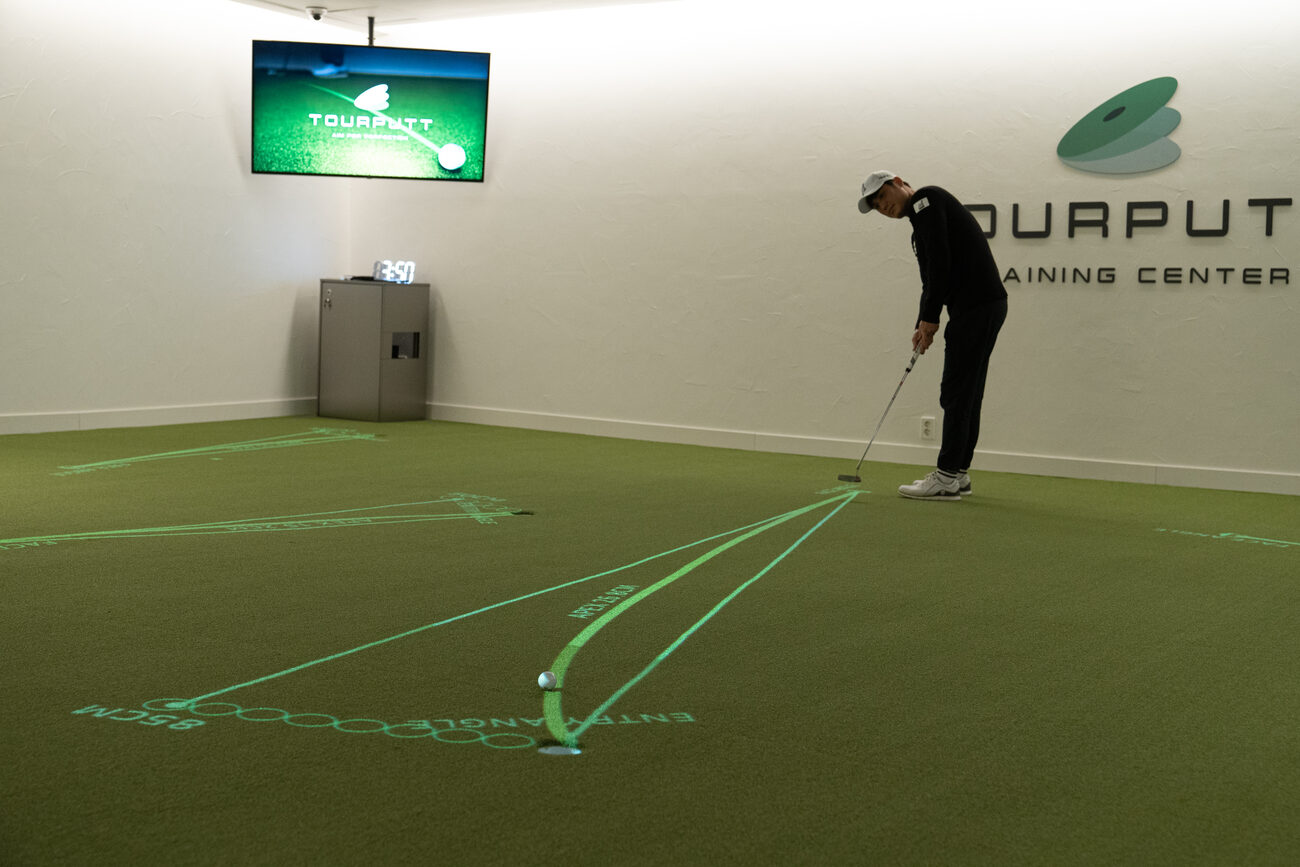 A golfer putts at the TOURPUTT Training Center, with the projected lines of the putt running across the green to the hole