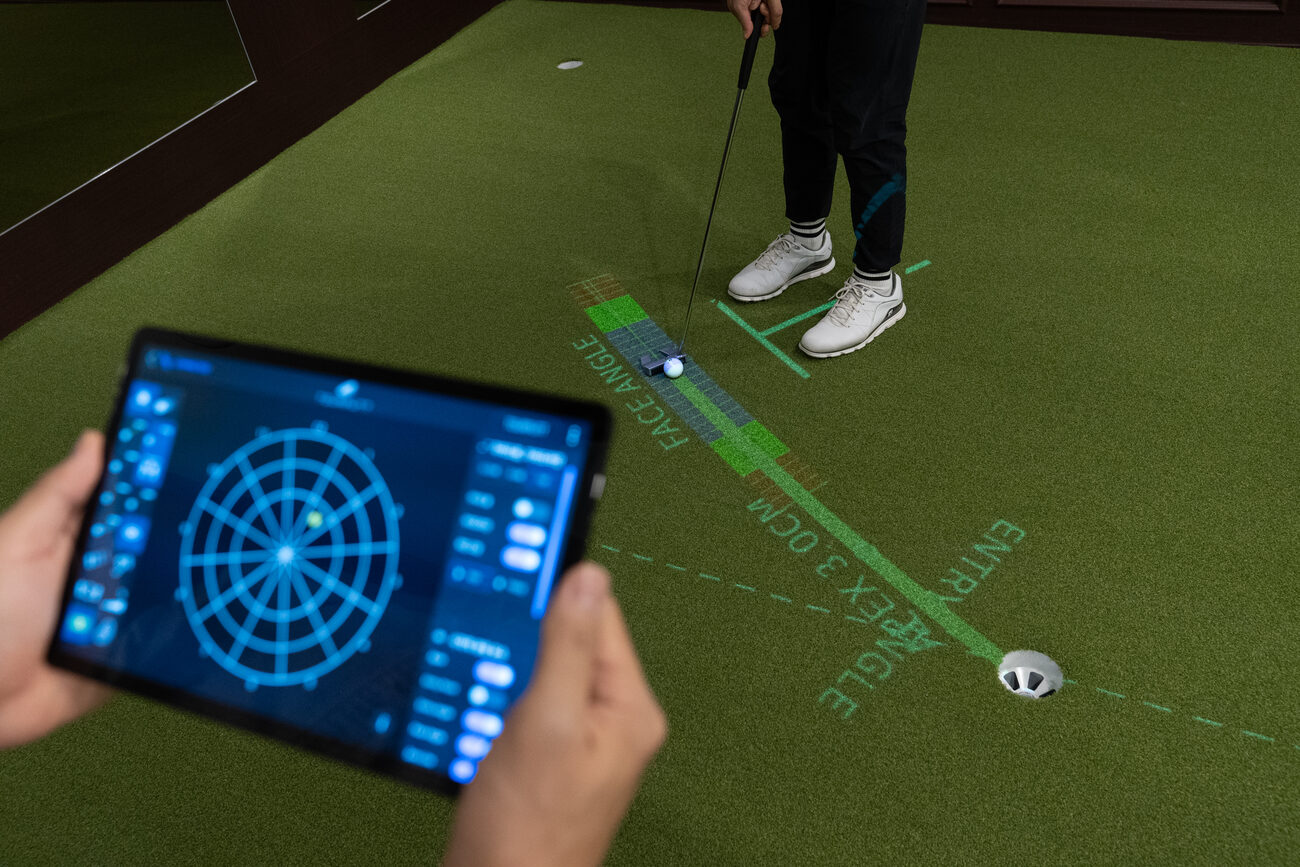 A tablet showing the Pattern Test chart, held above a green where a golfer putts along a projected line