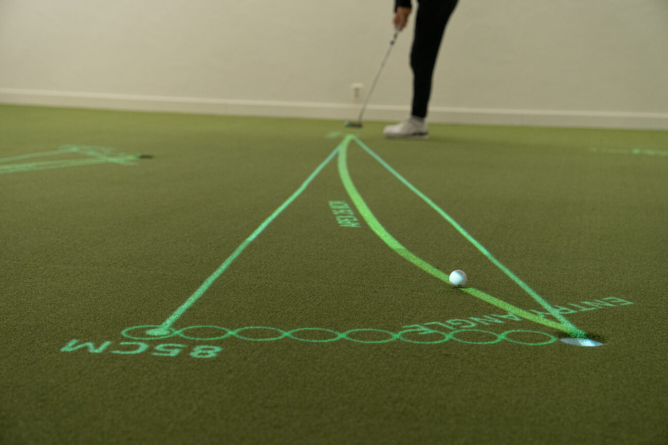 A ball rolling toward the hole between three projected lines that fan out from the putter, with an 85 cm aim marker beside the hole