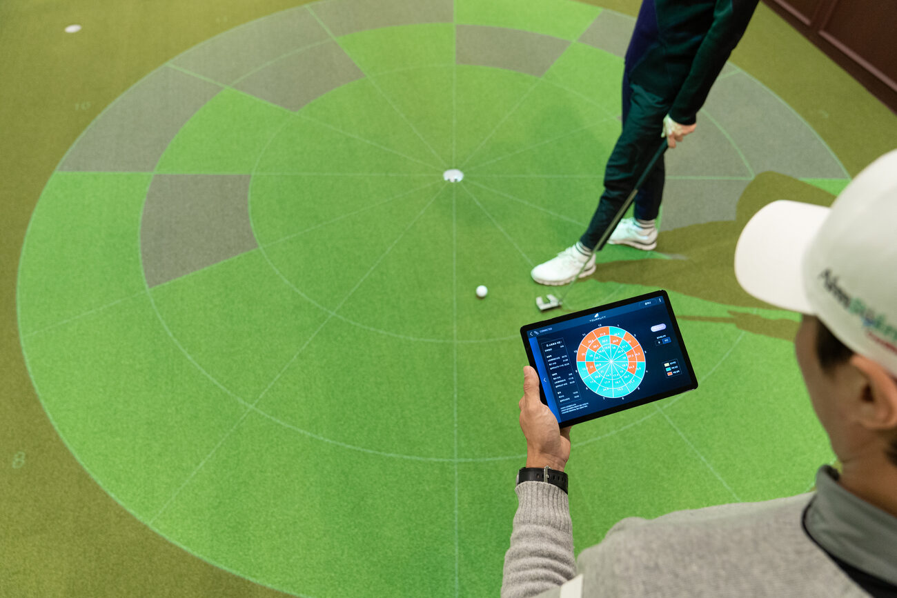 A coach holds a tablet showing Pattern Test results while a golfer putts across a ring of projected zones