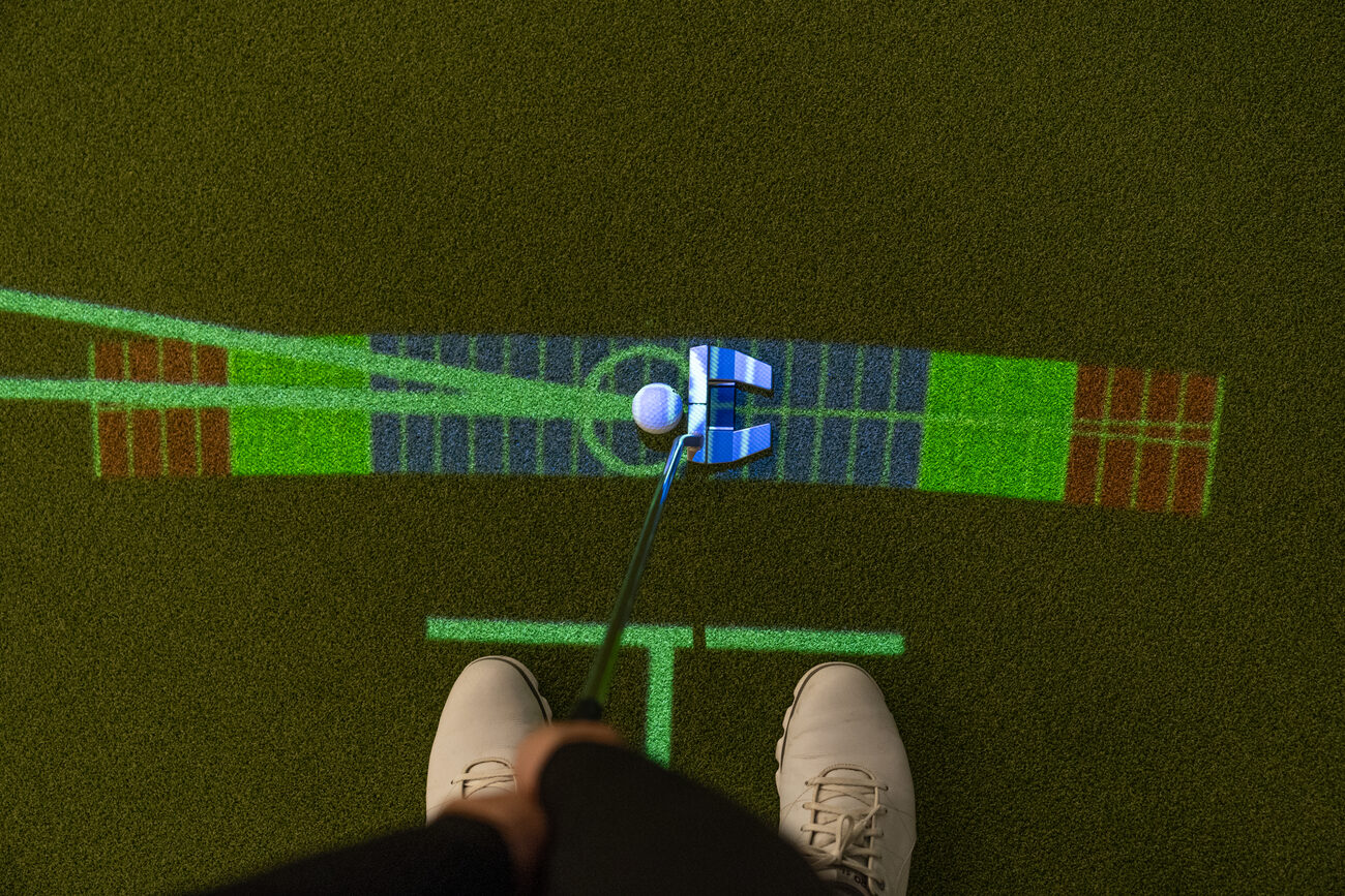 Seen from above: a putter behind the ball on a colour-banded guide projected along the path of the stroke